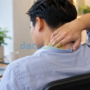 Pria memegang leher dengan ekspresi nyeri sambil duduk di sofa